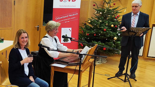 Zwei Musikerinnen und ein Redner am Pult, im Hintergrund ein Weihnachtsbaum