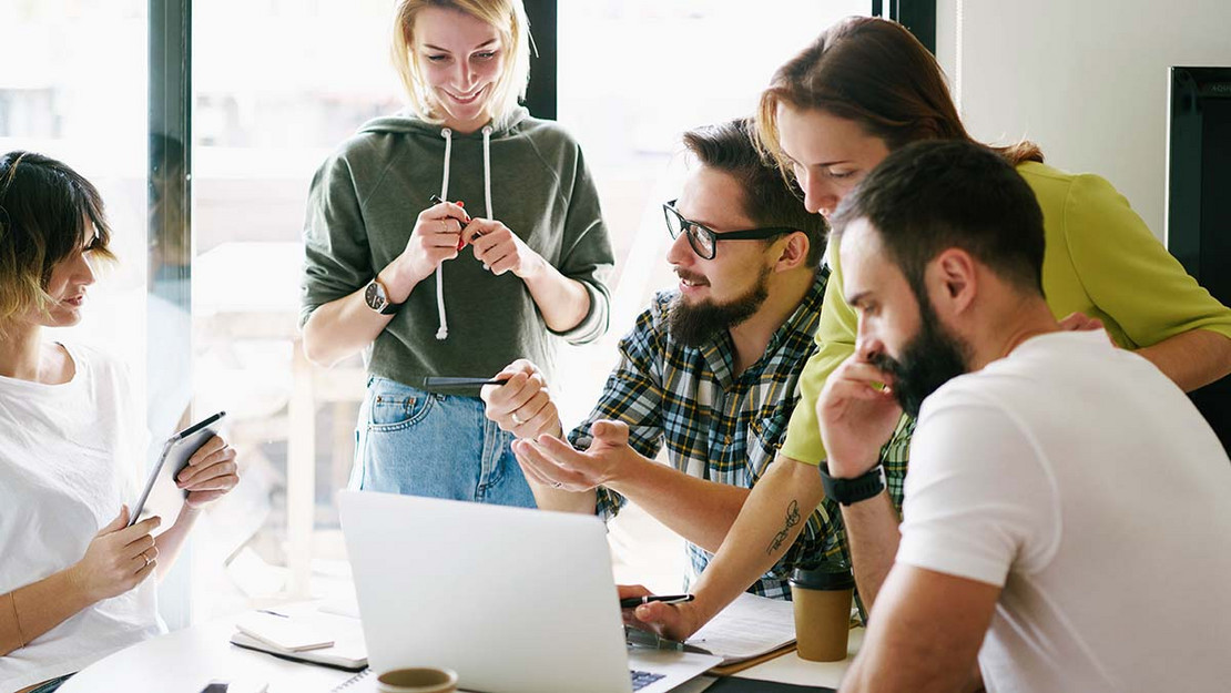 Eine Gruppe junger Menschen sitzt im Büro vor einem Laptop und diskutiert miteinander. 