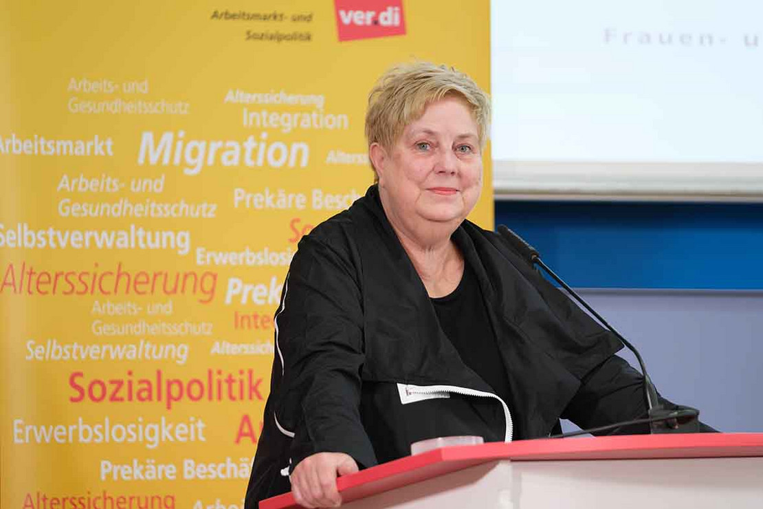 Frau steht vor einem gelbem Aufsteller am Mikrofon.