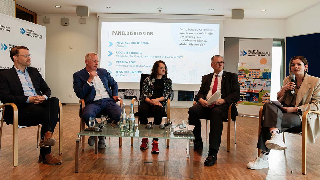 Fünf Personen sitzen auf Stühlen in einem Halbkreis, hinter ihnen eine Projektion des Veranstaltungstitels. 