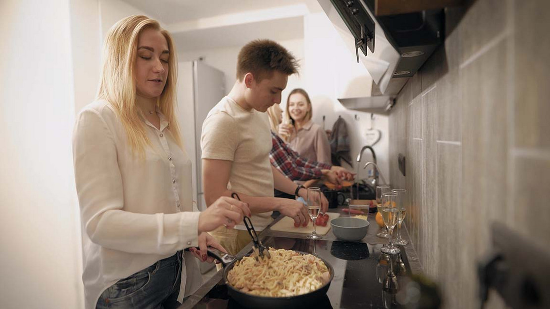 Drei junge Menschen kochen zusammen in einer Küche. 