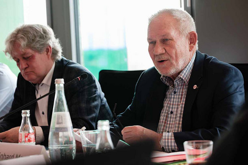 Zwei Personen sitzen an einem Tisch und haben Mikrofone vor sich. 