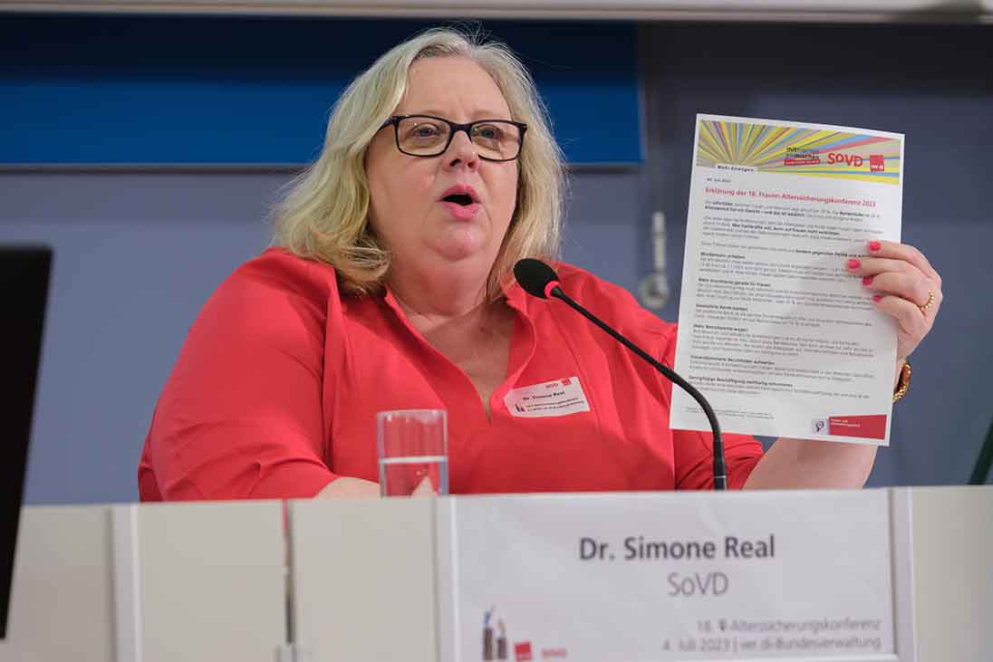 Frau am Mikrofon hält ein Papier hoch.