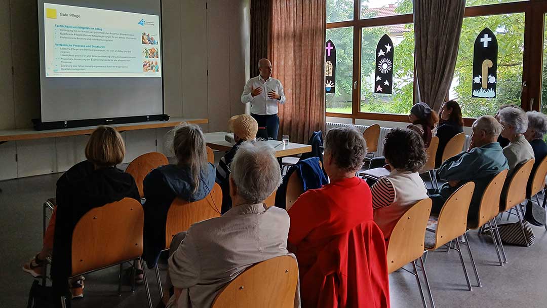 Menschen sitzen im Saal und schauen auf eine Leinwand.