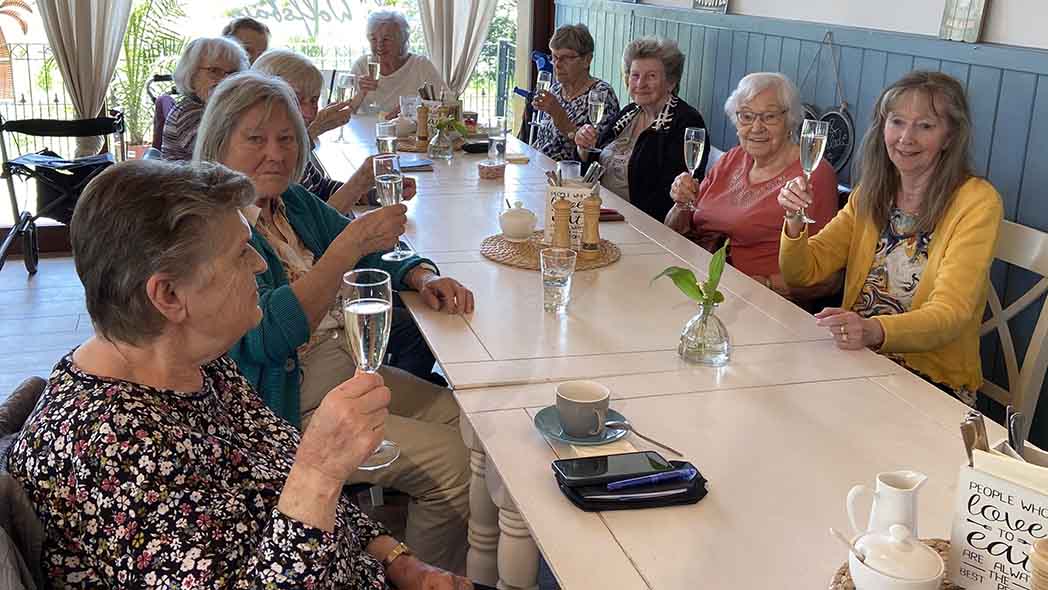 Menschen sitzen am Tisch und stoßen mit Sekt an.