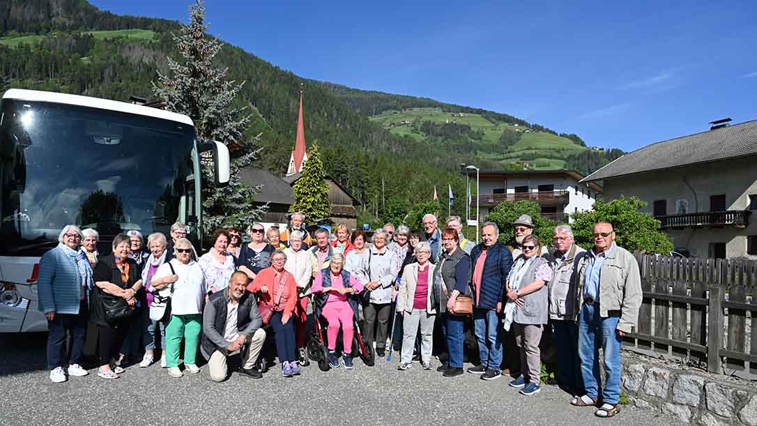 Gruppe vor Reisebus mit Bergpanorama.